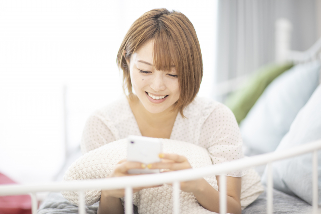 横になり笑顔でスマホを扱う女性