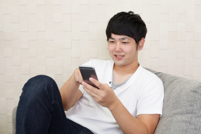 ソファの上でスマホを見てくつろぐ男性