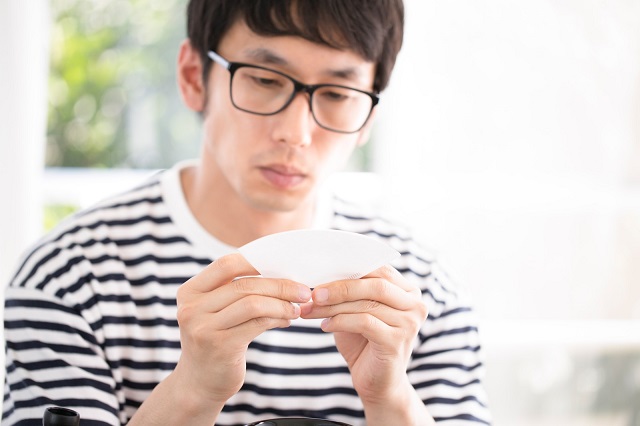 ドリップコーヒーのペーパーフィルタを丁寧に折るマメな男性