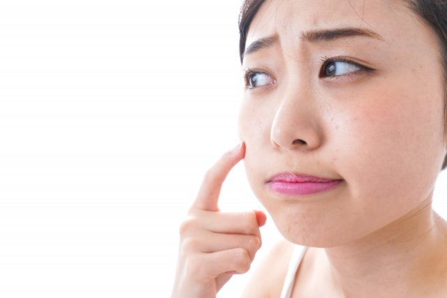 頬のニキビ跡を押さえしかめっ面の女性