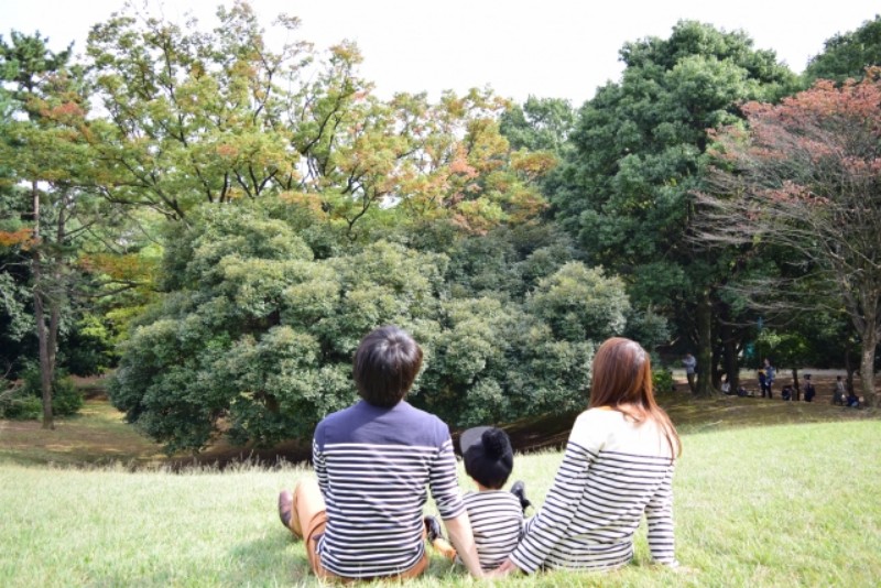芝生の上で背を向けて木や空を見ている親子3人