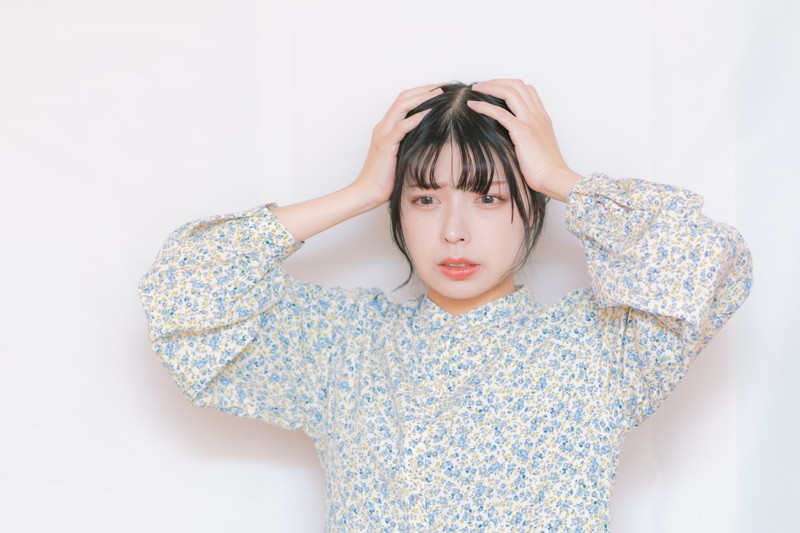 白い生地に青の小花柄の洋服を着て両手で頭を抱え焦る女性